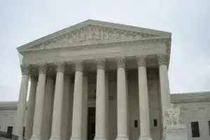 The image shows the front of a large, classical-style courthouse with tall columns and a triangular pediment, resembling the United States Supreme Court building. The sky is overcast.
