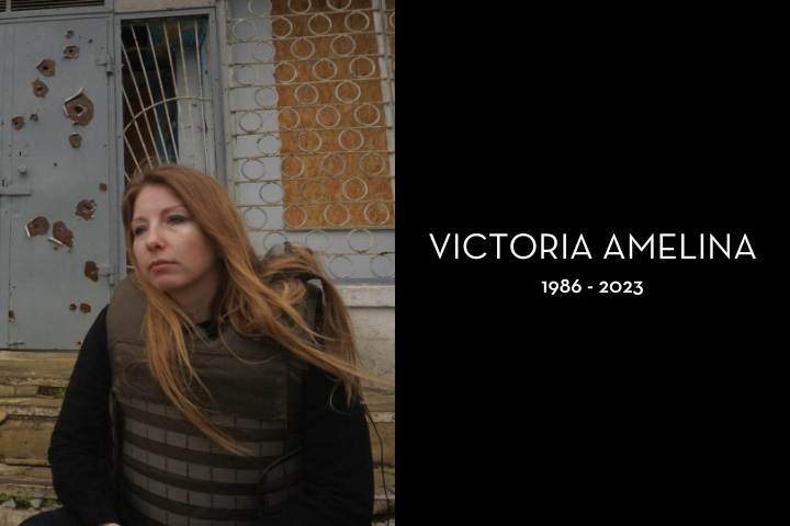 A woman with long hair wearing a protective vest sits in front of a damaged, bullet-ridden building. Beside her, text reads VICTORIA AMELINA 1986 - 2023 on a black background.