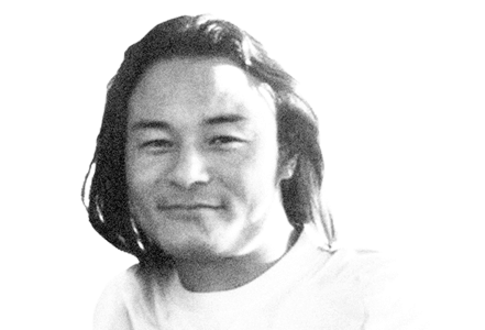 A black-and-white photo of a person with long, dark hair wearing a light-colored shirt, smiling slightly, and looking at the camera against a plain white background.