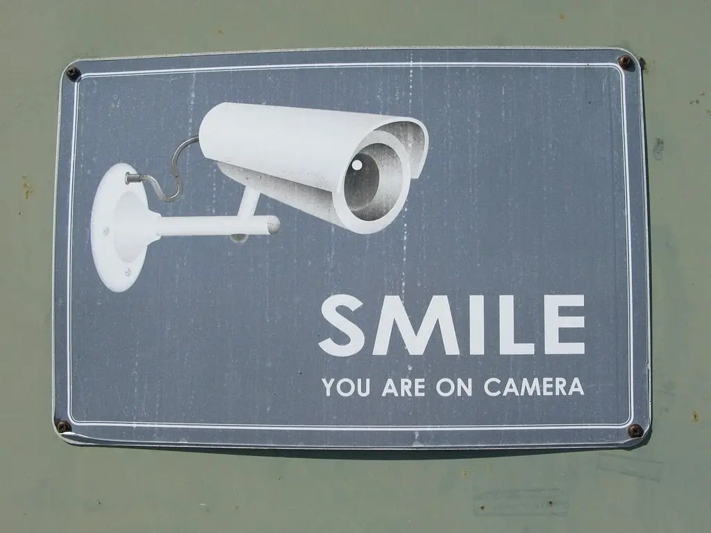 A sign with an illustration of a security camera and the text SMILE YOU ARE ON CAMERA on a gray background.