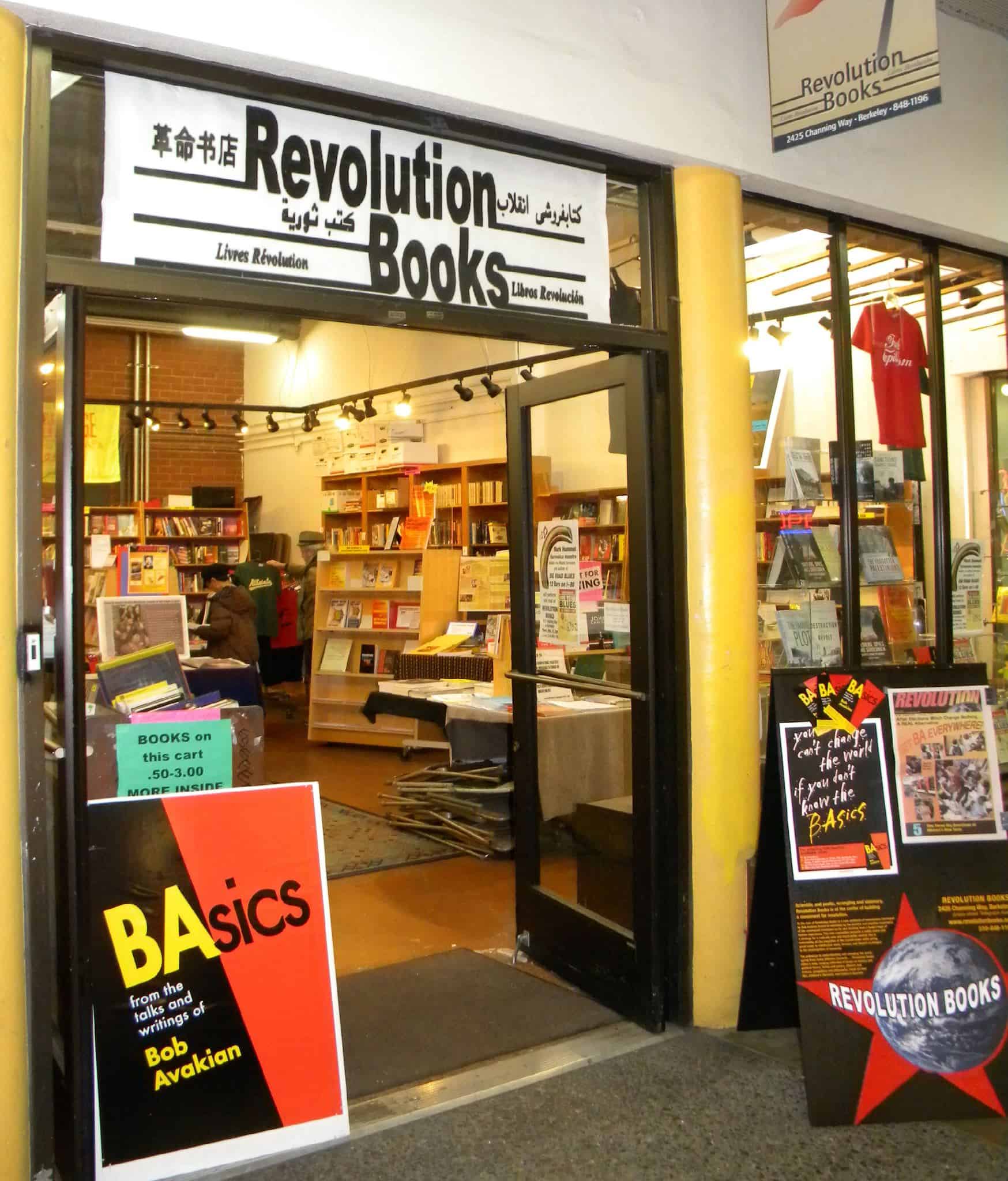 The entrance to Revolution Books features open doors, books and displays inside, and signs promoting “BAsics” by Bob Avakian. Posters and shelves filled with books are visible through the doorway.