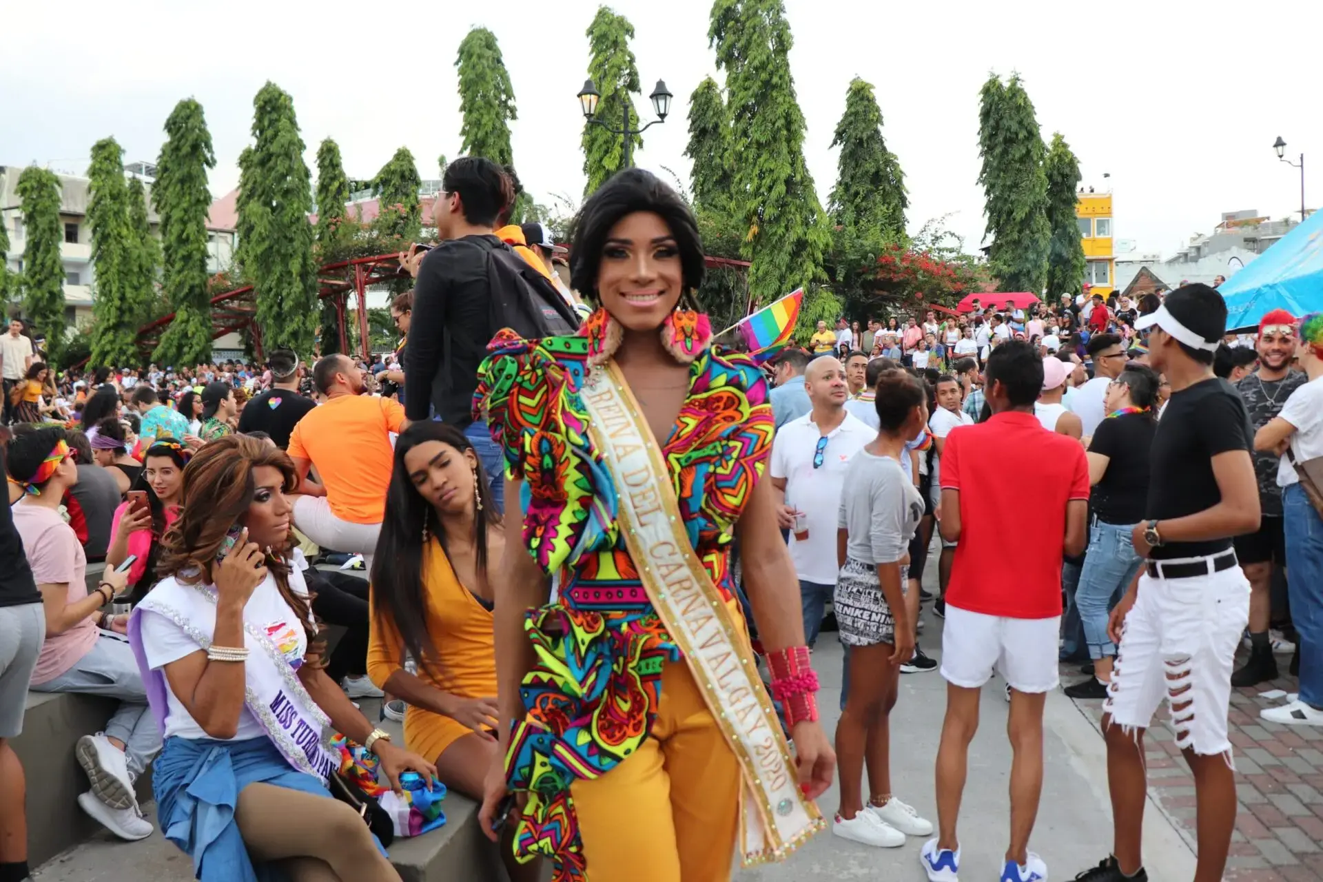 A woman in a colorful outfit with a sash and a crowd of people.