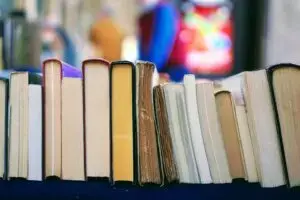 A row of books standing upright with their spines and pages facing outward, displayed on a table with a blurred background.