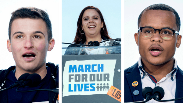 Three young people speak at microphones. The center speaker stands behind a podium with a “March For Our Lives” sign. All three look engaged, addressing an audience, with clear skies in the background.