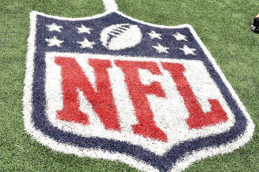 The NFL logo painted on green turf, featuring a football and white stars above the large red letters NFL inside a blue shield outline.