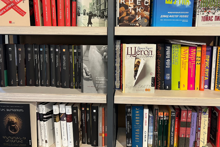 Bookshelves filled with various books in different languages and colors, including Russian and Armenian titles, with some books stacked vertically and others placed horizontally.