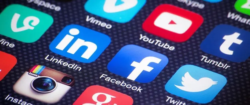 Close-up of a smartphone screen displaying various social media app icons, including LinkedIn, Facebook, Twitter, Instagram, YouTube, Tumblr, and Vimeo, against a dark, dotted background.