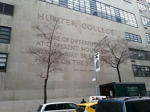 The exterior wall of Hunter College displays a large quote by Ralph Waldo Emerson. Leafless trees, a green truck, and yellow taxis are visible along the street in front of the building.
