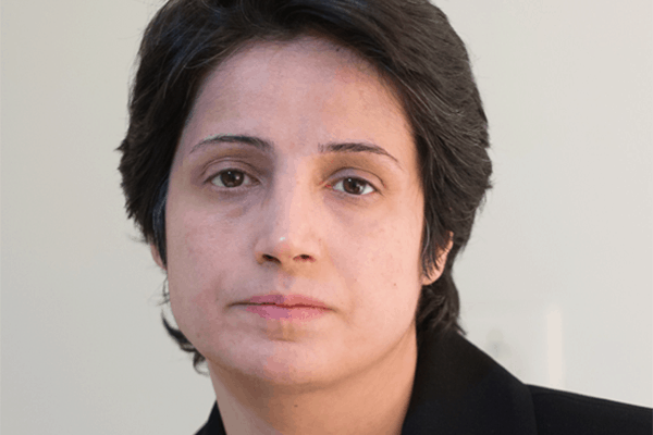 A person with short dark hair and a neutral expression, wearing a black jacket, looks directly at the camera against a light-colored background—echoing the quiet strength of Iranian political prisoners like Nasrin Sotoudeh seeking release.