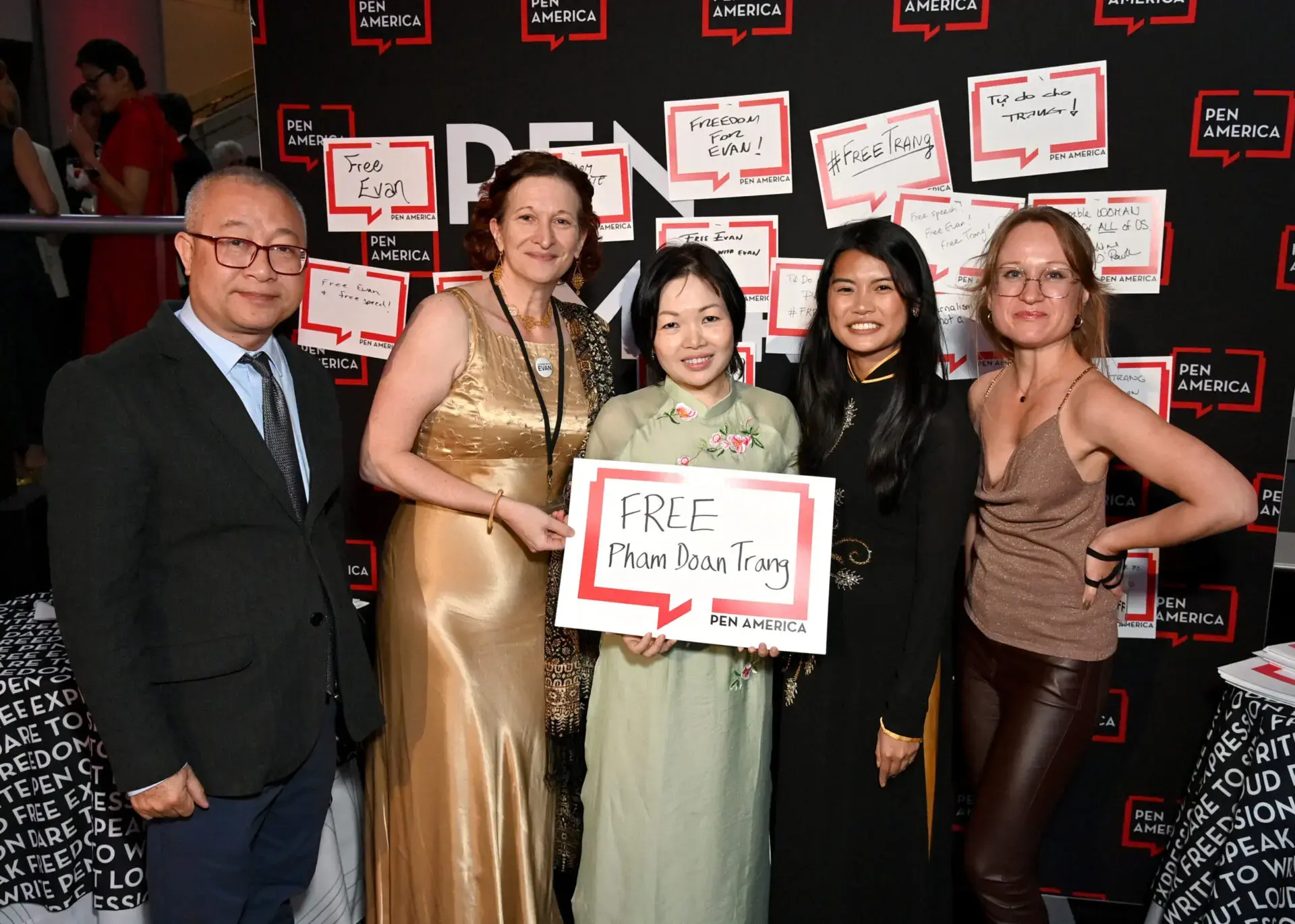 Five people stand together at a PEN America event, holding a sign that reads FREE Pham Doan Trang. The background features multiple similar signs calling for the release of various individuals.