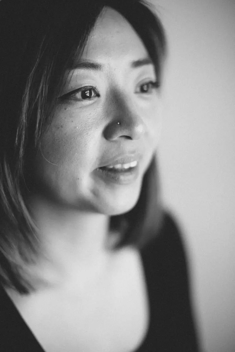 Black and white close-up portrait of a woman with straight hair, a nose piercing, and a soft smile, looking slightly away from the camera with a gentle expression.