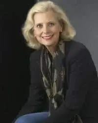 A smiling woman with blond hair, wearing a dark blazer and patterned scarf, poses against a dark background.