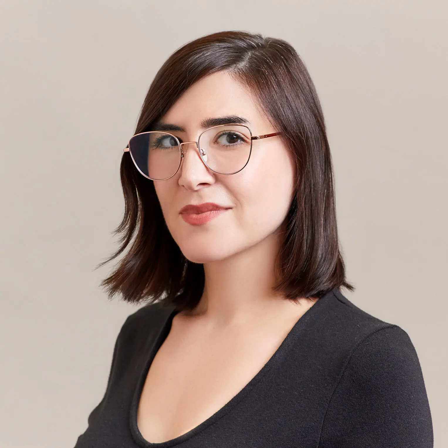 A woman with straight, shoulder-length brown hair and glasses, wearing a black top, looks confidently at the camera against a plain light background.