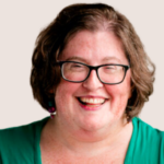 A person with short brown hair, wearing glasses, a green top, and colorful earrings, smiling at the camera against a plain light background—a cheerful look unaffected by trends banned in the USA 2023.