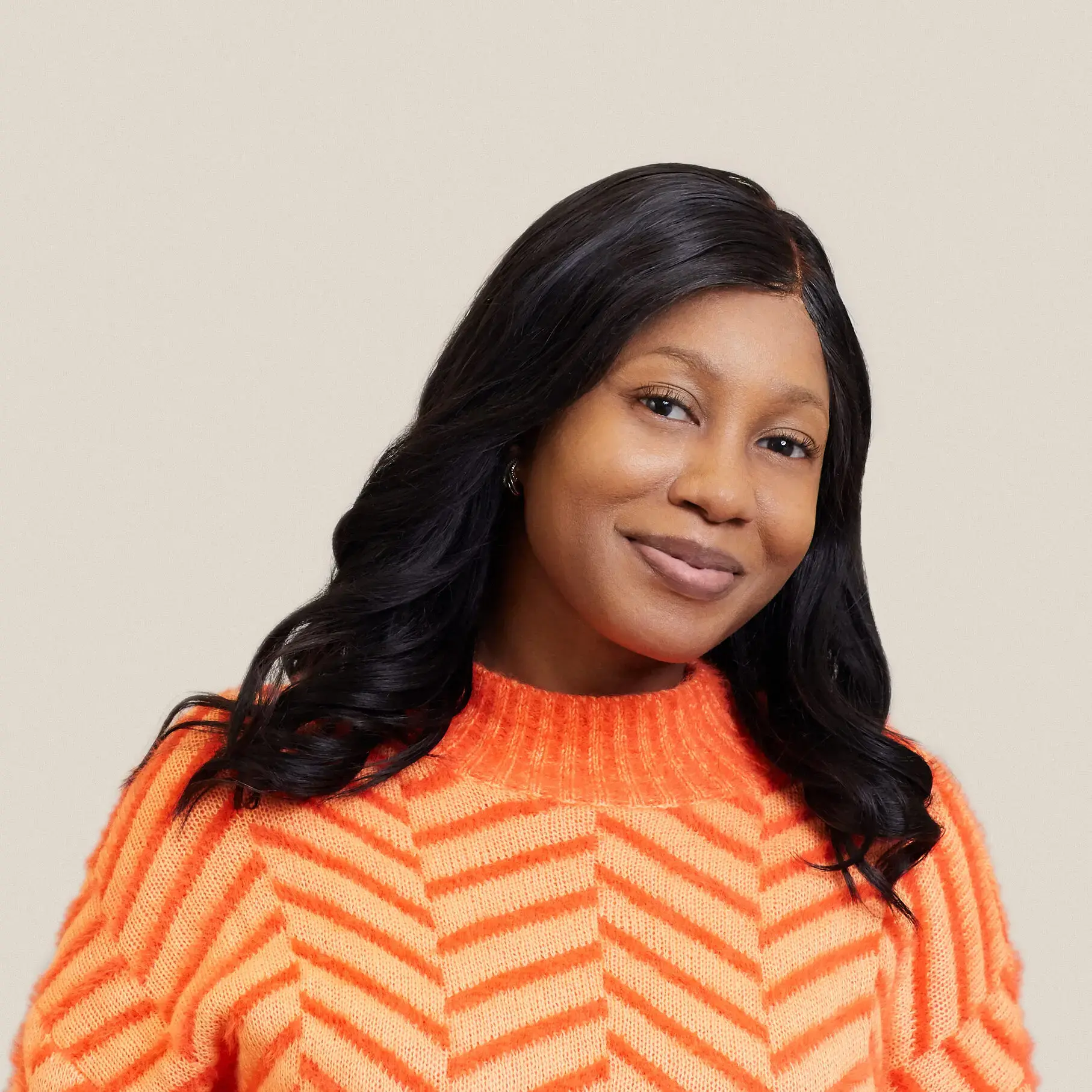 A woman with long black hair wearing an orange and light pink striped sweater smiles gently at the camera against a plain light beige background.