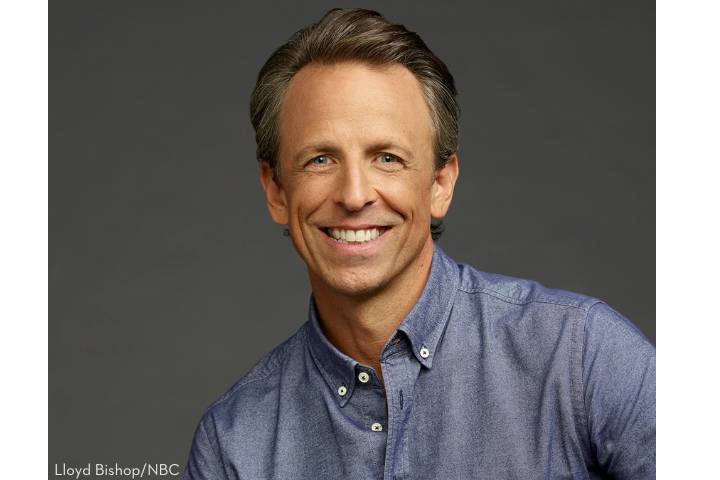 A smiling man with short, light brown hair wearing a blue button-up shirt poses in front of a plain dark gray background. Photo credit: Lloyd Bishop/NBC.