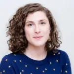 A woman with short, curly brown hair is wearing gold earrings and a navy blue sweater with a yellow star pattern. She looks at the camera with a neutral expression, highlighting the importance of digital safety in facing online abuse.