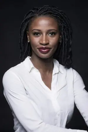 A woman with dark braided hair and wearing a white blouse poses against a black background, smiling softly at the camera.