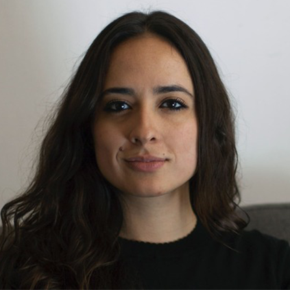 A woman with long, wavy brown hair and a neutral expression looks directly at the camera, highlighting themes of online abuse and digital safety. She is wearing a black top, and the background is plain and light-colored.