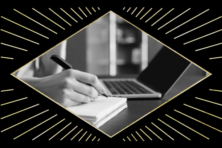 Black and white image of a hand writing in a notebook, possibly noting ideas for literary grants, next to an open laptop on a desk. The photo is framed by a diamond-shaped design with radiating lines.