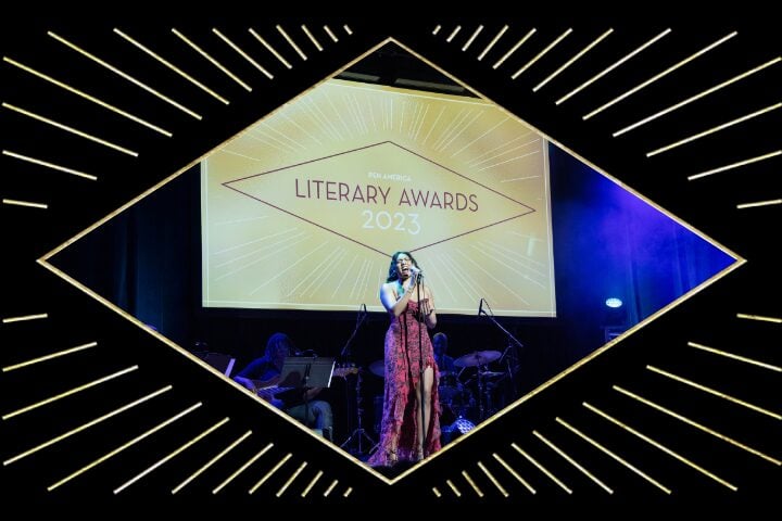 A woman in a red dress sings on stage at the Literary Awards 2023, with musicians playing behind her and decorative gold lines elegantly framing the scene.