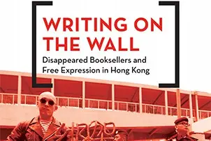 The book cover titled Writing on the Wall: Disappeared Booksellers and Free Expression in Hong Kong captures a powerful image of two men set against a red-tinted building, evoking the intense atmosphere surrounding free expression in Hong Kong.