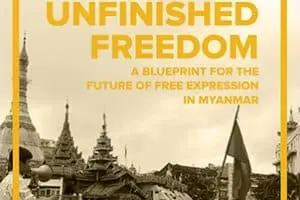 The cover of Unfinished Freedom presents a sepia-toned image of a bustling Myanmar street adorned with traditional architecture. A crowd waves flags, underscoring the theme: A Blueprint for the Future of Free Expression in Myanmar.