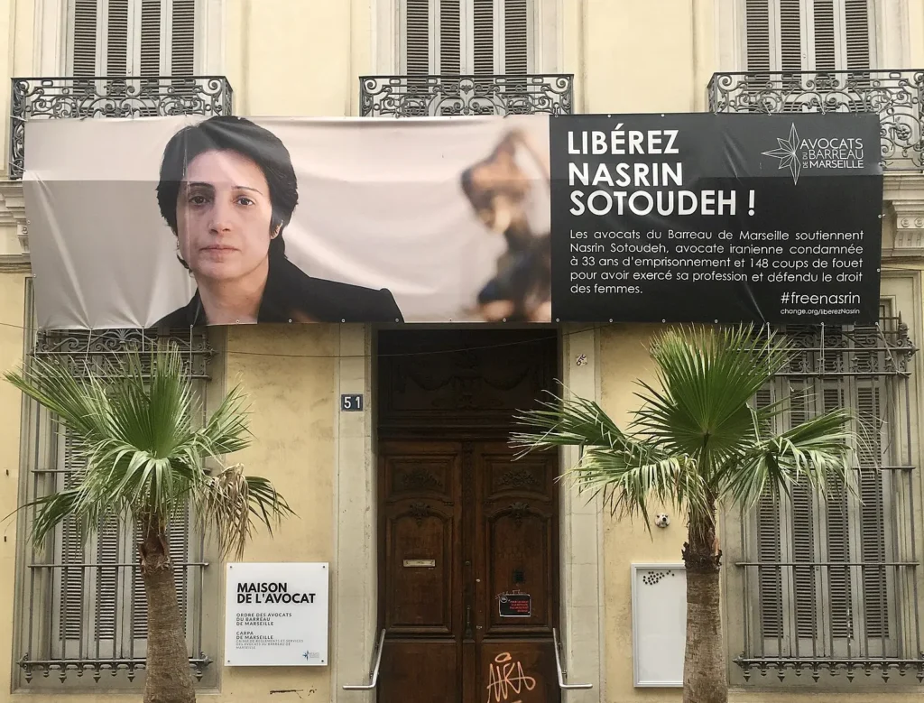 A banner above a building entrance shows a woman's portrait and "Libérez Nasrin Sotoudeh!" in French, advocating for her release. As noted in the Freedom to Write Index 2020, two palm trees stand in front of the doorway.