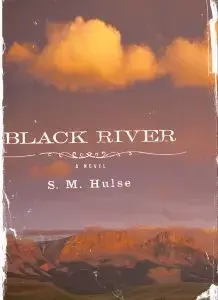 Cover of the book Black River by S.M. Hulse, reminiscent of an Ottessa Moshfegh aesthetic. The image captures a rugged landscape under orange-tinged clouds, with the title and authors name in white text over the scene. The cover boasts a worn, vintage look with scuffed edges.