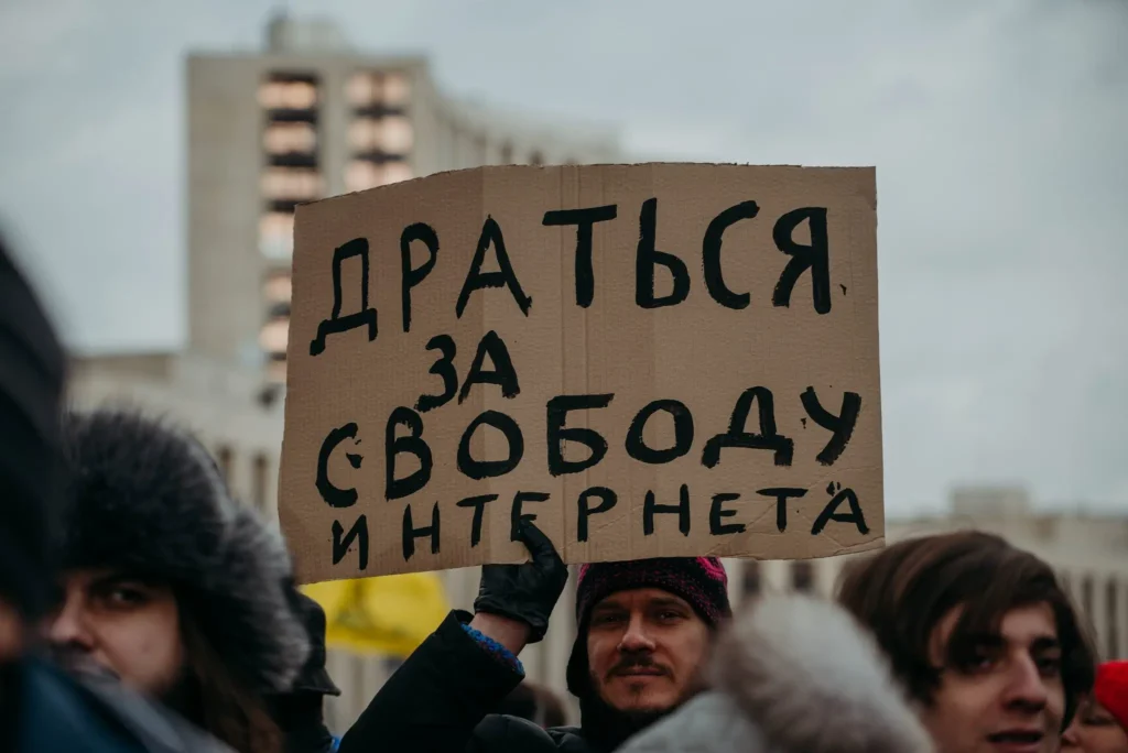 A person holds a cardboard sign in Russian reading Драться за свободу интернета (Fight for internet freedom) during a protest, highlighting concerns over digital sovereignty, with buildings and other protesters visible in the background.