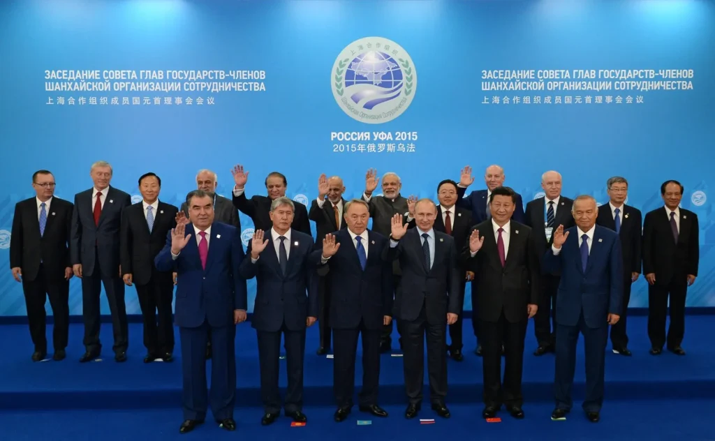 A group of world leaders in suits stands on a stage, posing for a group photo at the 2015 SCO summit in Russia. Most are raising their right hand in greeting; a blue backdrop highlighting digital sovereignty displays the event's name in Russian and Chinese.
