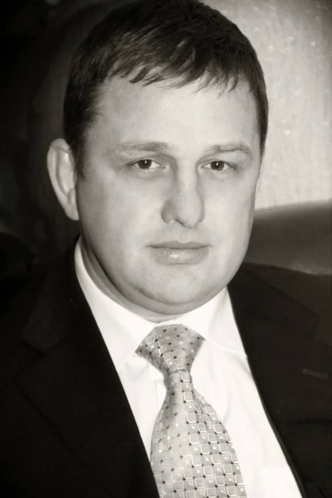 A man in a suit and patterned tie sits in a chair, looking at the camera with a neutral expression. The black-and-white image reflects the timeless elegance often associated with Ukrainian culture.