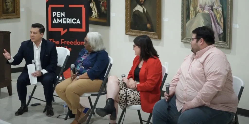 Four people sit in chairs holding microphones, participating in a panel discussion on fighting disinformation locally. Three face the man on the far left, who is speaking. A PEN America banner stands behind them and framed artworks hang on the wall.