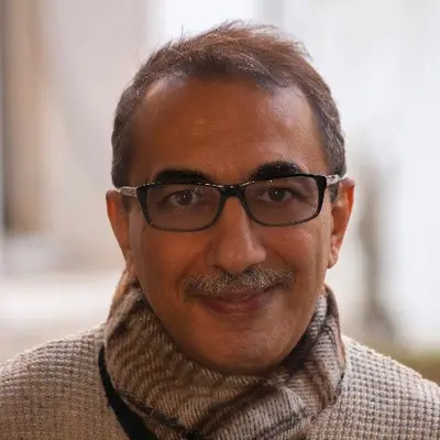 A middle-aged man with short hair, glasses, and a mustache smiles at the camera. He is wearing a light sweater and striped scarf, with a softly blurred, neutral background—an image featured in the Freedom to Write Index 2022.