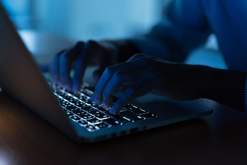 Close-up of a person’s hands typing on a laptop keyboard in low light, with the keys illuminated by the laptop’s backlight.