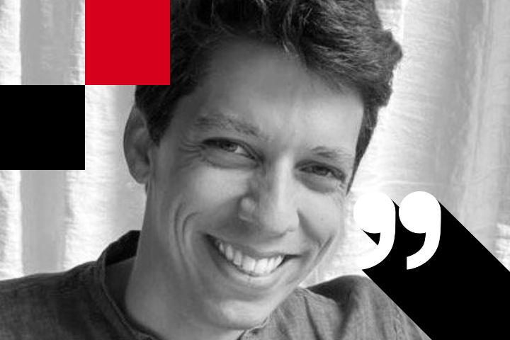 Black and white photo of a smiling person with short hair. A large white quotation mark symbol is in the bottom right corner, partially on the person. Red and black geometric shapes appear in the top left. A curtain is in the background.