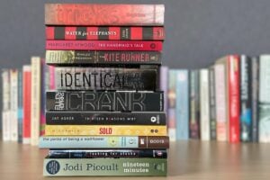 A vertical stack of books with visible titles, including Water for Elephants, The Handmaids Tale, and The Kite Runner, showcases thought-provoking stories often found on the banned books list 2024, alongside Crank and Thirteen Reasons Why.