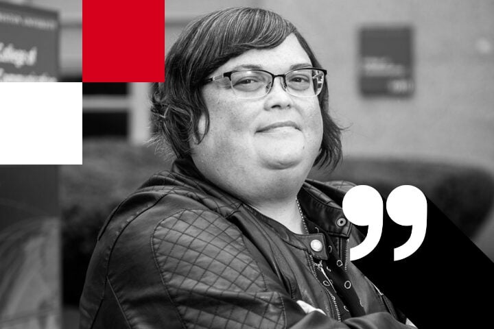 A person with glasses and short hair smiles while looking slightly upwards. They are wearing a quilted jacket. The image is overlaid with artistic elements: red and white rectangles and large quote marks. The background is blurred.