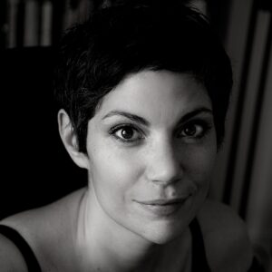 Black and white portrait of a person with short hair, looking at the camera with a slight smile. The background is softly blurred.