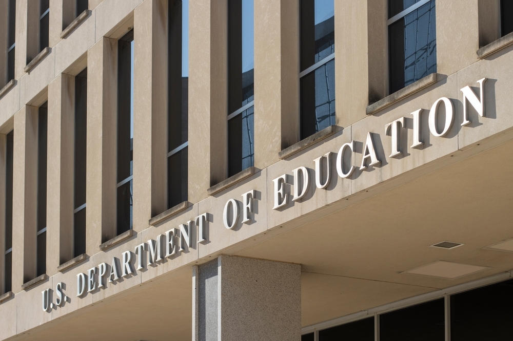 The image depicts the exterior of a building with large, bold letters reading U.S. Department of Education. Constructed from concrete and featuring numerous rectangular windows, this building represents a symbol in the ongoing debate over educational censorship.