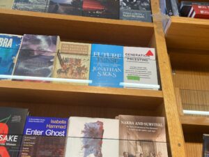 Wooden bookshelves displaying various books, including titles like The Travels of Ibn Battutah, Future Tense, Generation Palestine, and Nakba and Survival.