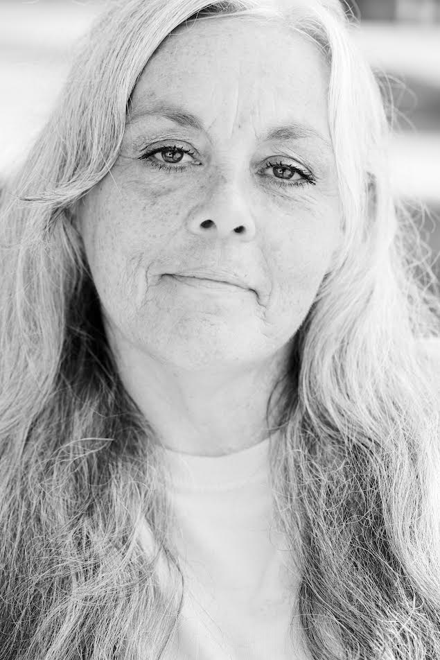 Black and white portrait of a woman with long, light-colored hair and a calm expression, wearing a light top. The background is softly blurred.
