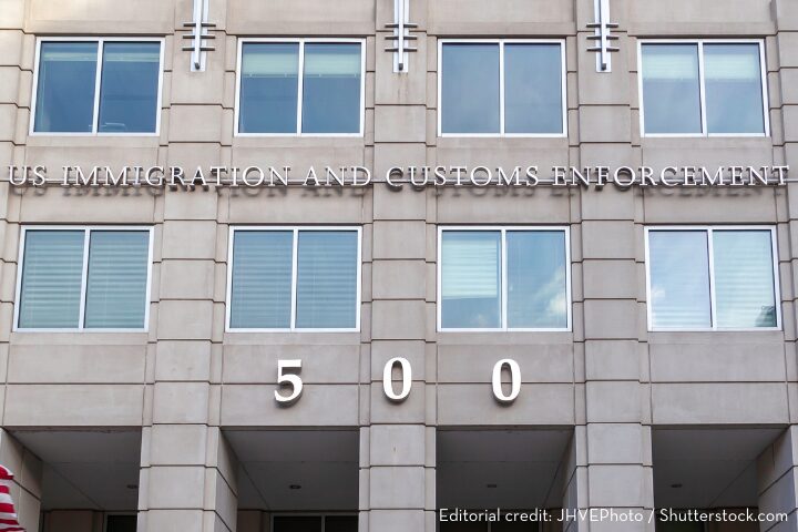 The facade of a building displaying U.S. Immigration and Customs Enforcement above windows and the number 500 below. The structure has large square windows and a stone exterior.