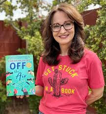 A person with long brown hair and glasses smiles while holding a book titled Off the Air. They wear a red shirt with a cactus and the words Get Stuck in a Book. The background features greenery and a wooden fence.