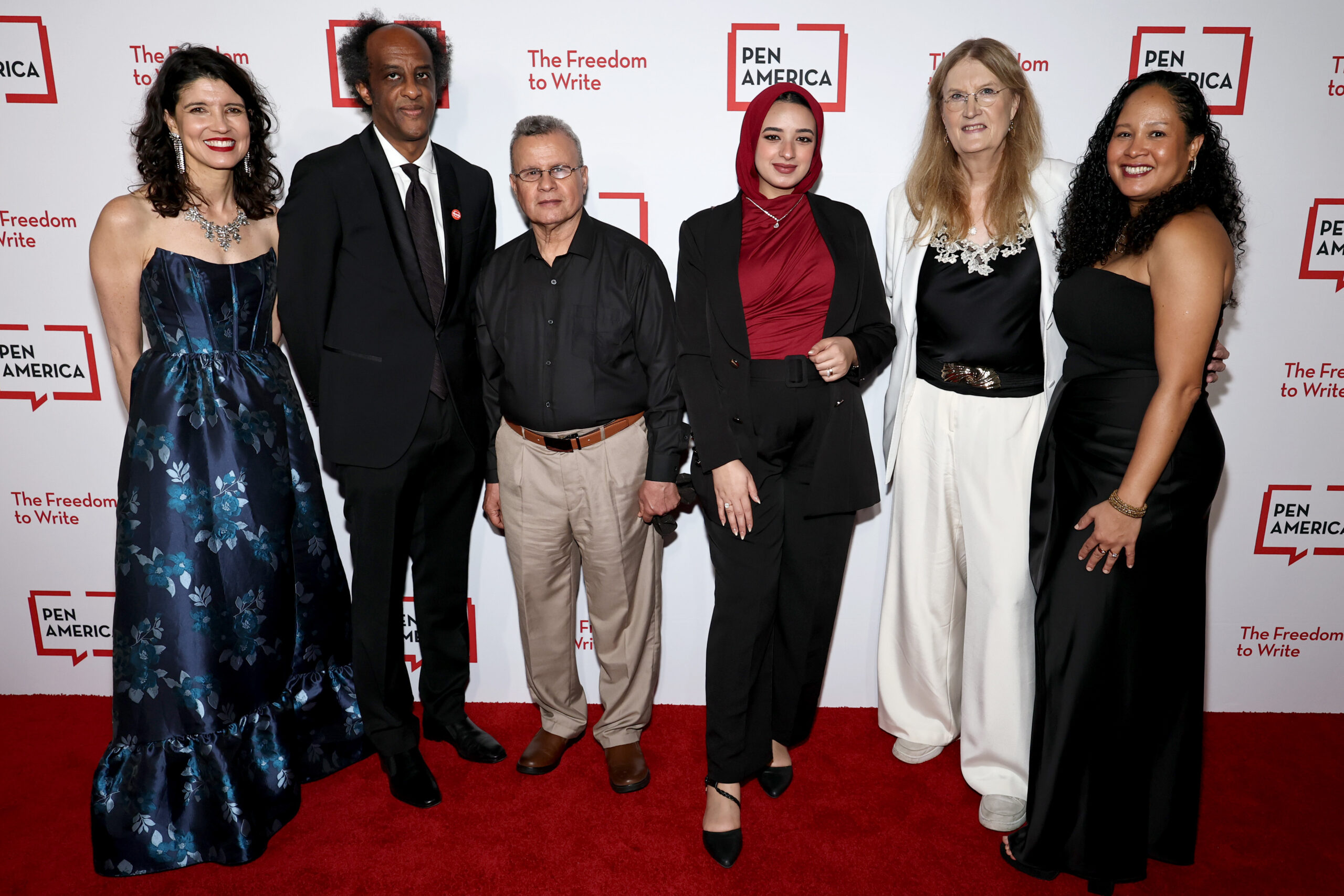 Six people stand together, smiling, on a red carpet in front of a PEN America backdrop that reads “The Freedom to Write.” The group is dressed in formal and semi-formal attire.