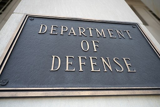 A metal plaque mounted on a stone wall displays the words Department of Defense in large, raised letters.