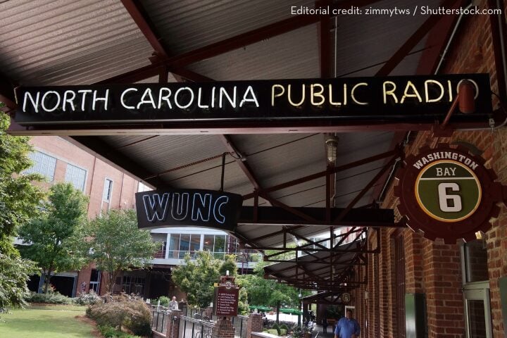 A sign under a metal awning reads “NORTH CAROLINA PUBLIC RADIO WUNC.” A green sign shows Washington Bay 6. Brick buildings and greenery are visible in the background.