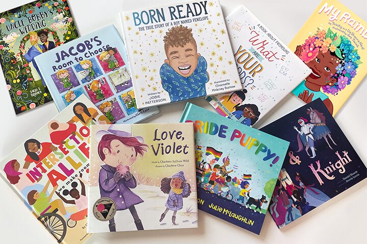 A selection of colorful children’s books are arranged on a white surface, featuring diverse characters and themes of inclusion, identity, and acceptance. Titles include “Love, Violet,” “Ride, Puppy!,” and “Intersection Allies.”.