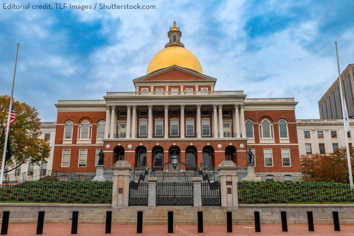 The Massachusetts State House in Boston, featuring a prominent golden dome, red brick facade, white columns, and a black iron fence under a partly cloudy sky.