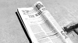 A folded copy of The Wall Street Journal newspaper lies on a flat, light-colored surface, with headlines and text visible in black and white.